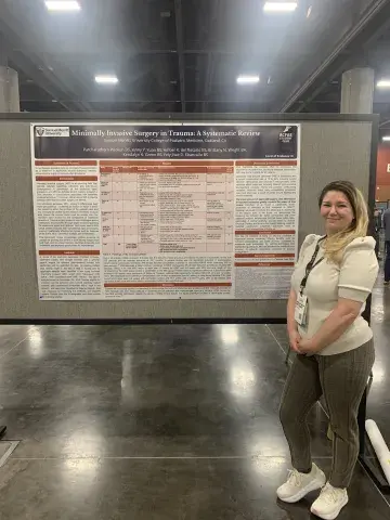 A student stands next to a large academic poster titled “Minimally Invasive Surgery in Trauma: A Systematic Review,” representing Samuel Merritt University’s College of Podiatric Medicine.