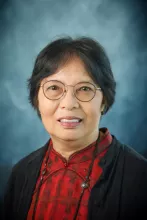 Headshot of woman with brown hair, glasses, and red shirt.
