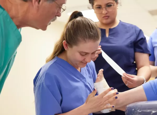 Student wrapping foot with Doctor observing