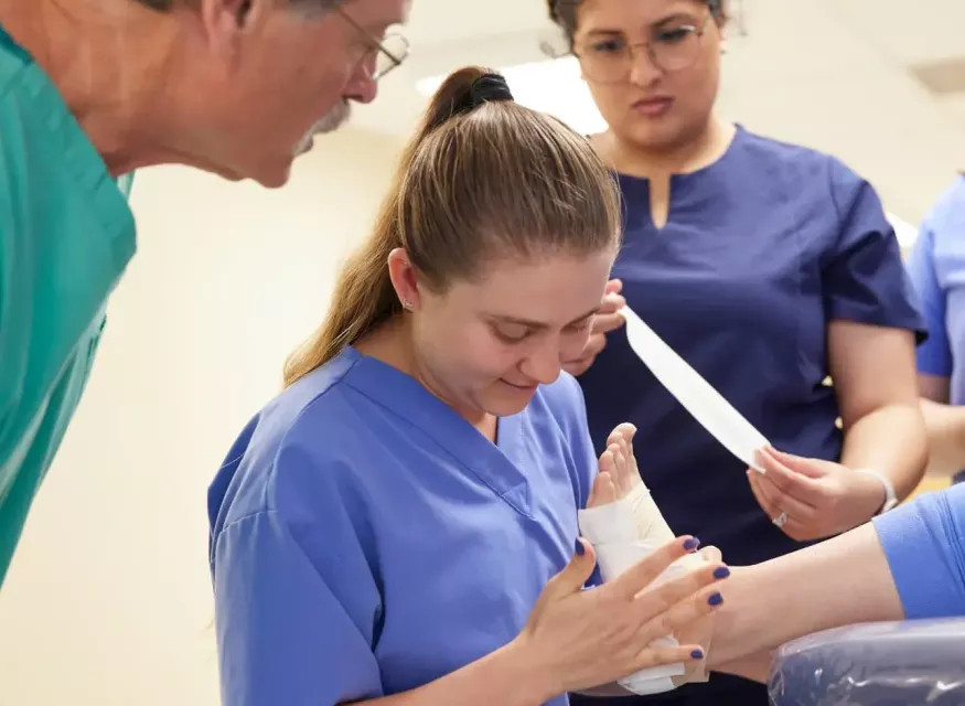 Student wrapping foot with Doctor observing