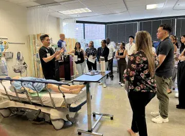 Nursing faculty and prospective students stand in simulation lab watching a demonstration.