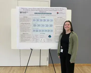Occupational Therapy student stands in front of poster with class project.