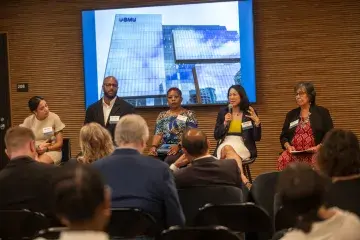 5 panelists on stage, one holds a microphone.