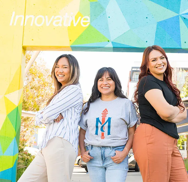 Students pose in front of Oakland campus mural.