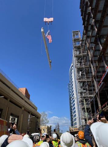 Onlookers in safety gear watch as the last beam is hoisted into the air.