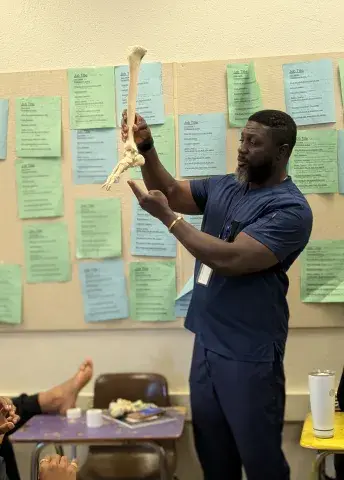 SMU member dressed in dark blue scrubs holds up leg and foot model as a teaching tool.