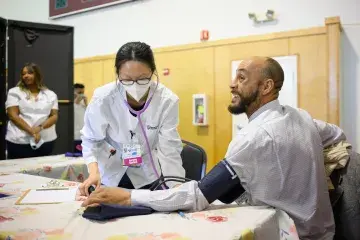 Nursing student with mask and white coat checks patient's blood pressure.