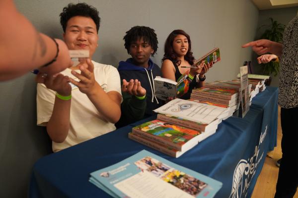 Students sit behind a table with books.