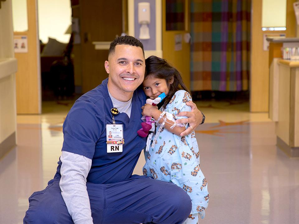 Alumnus Carter Todd poses with a child in hospital hallway