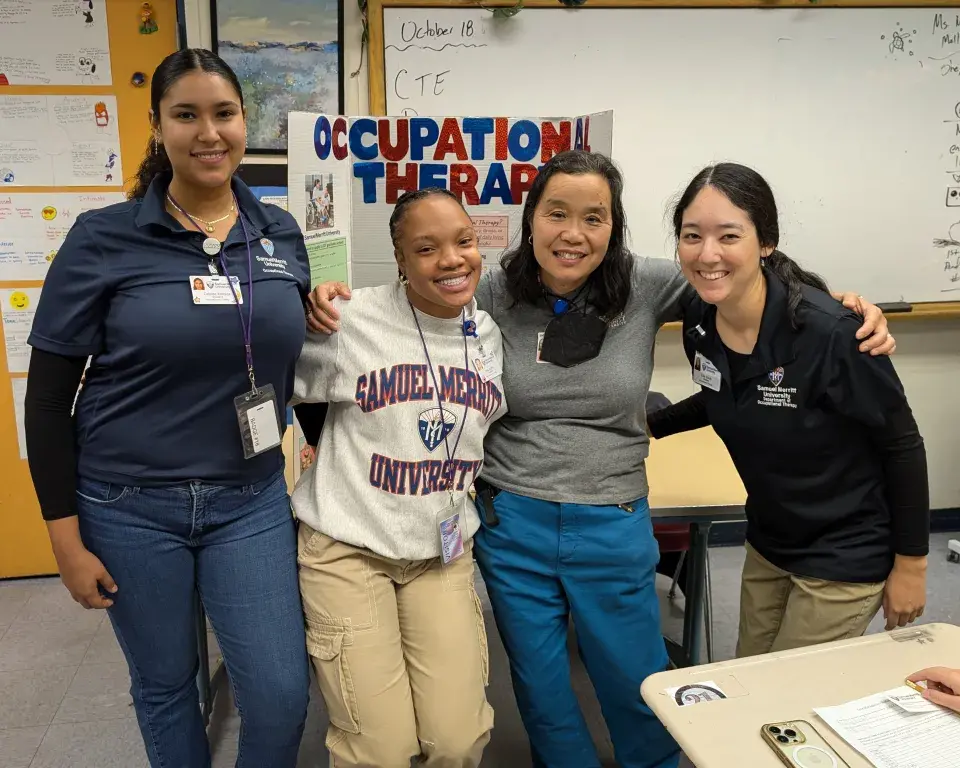 4 people in a classroom wearing SMU branded apparel with an "Occupational Therapy" sign in the background.